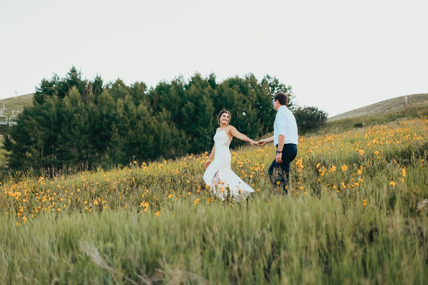 A couple dances in a wildflower meadow with mountains in the background.