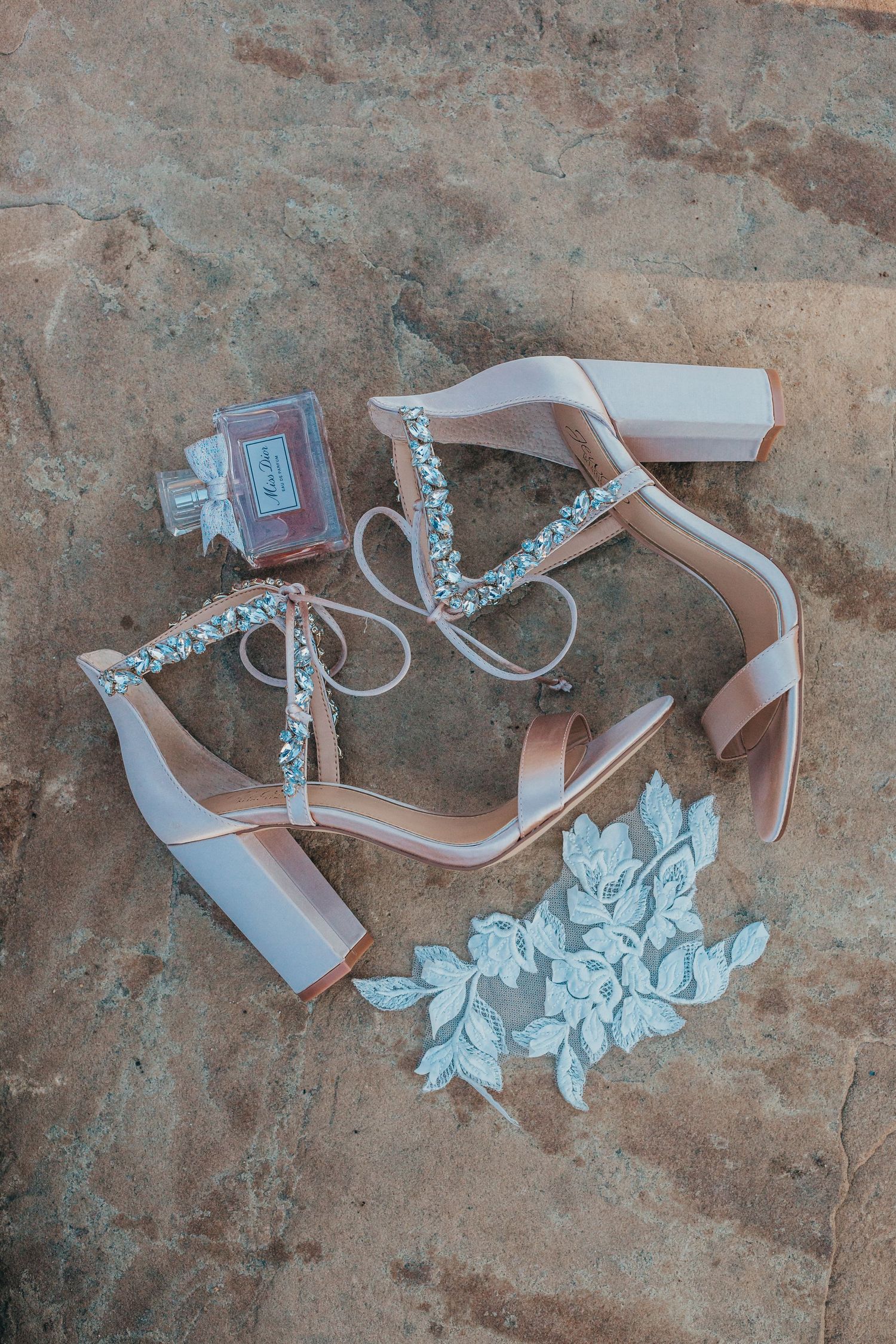 Elegant white wedding shoes with pearl details and lace appliques on stone surface.