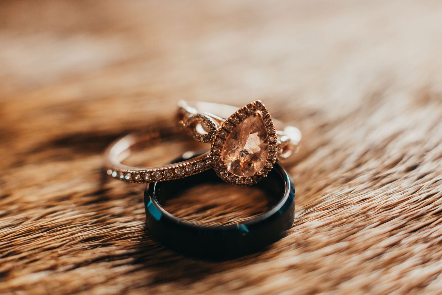 Rose gold engagement ring and blue wedding band photographed on textured brown surface.