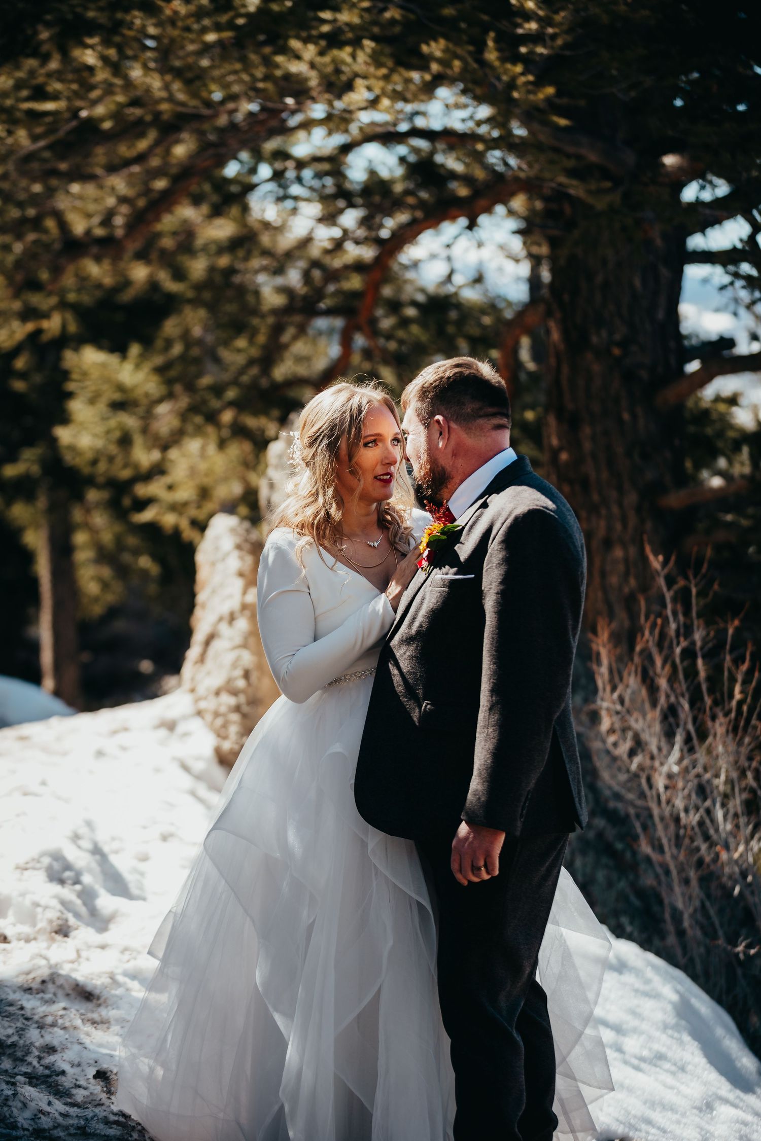 A romantic winter wedding portrait with snow and golden sunlight filtering through trees.