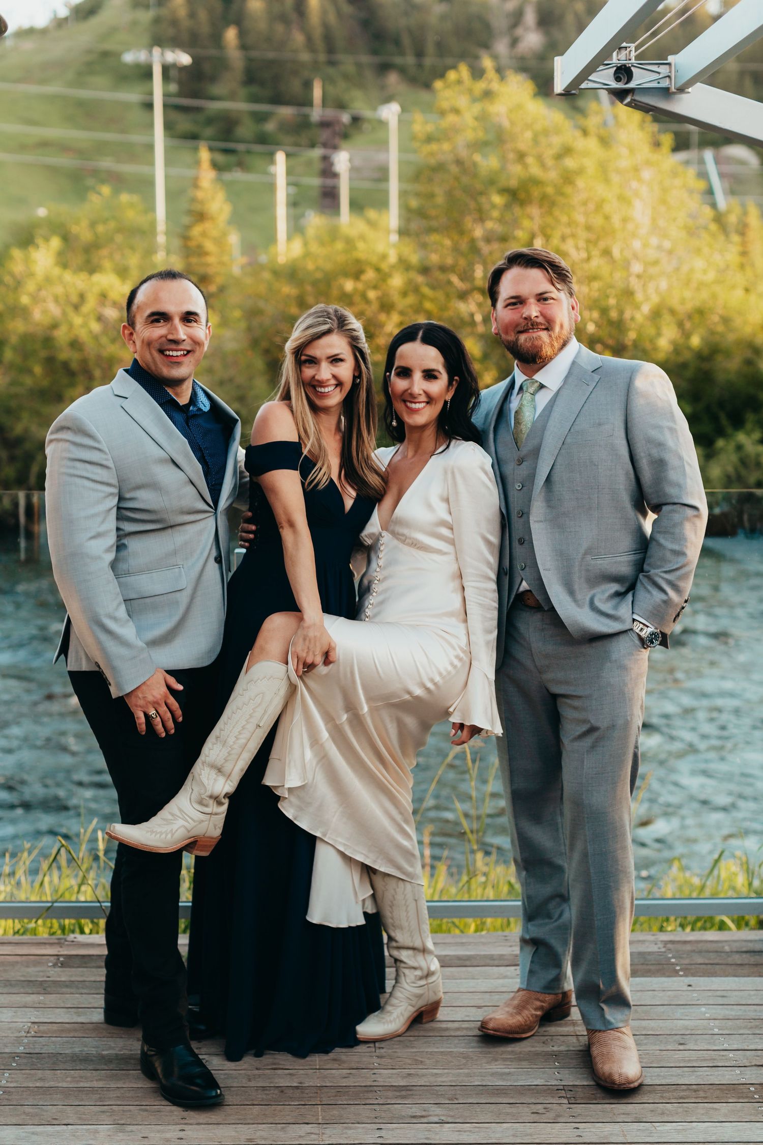 Wedding party poses on wooden deck with scenic mountain backdrop.