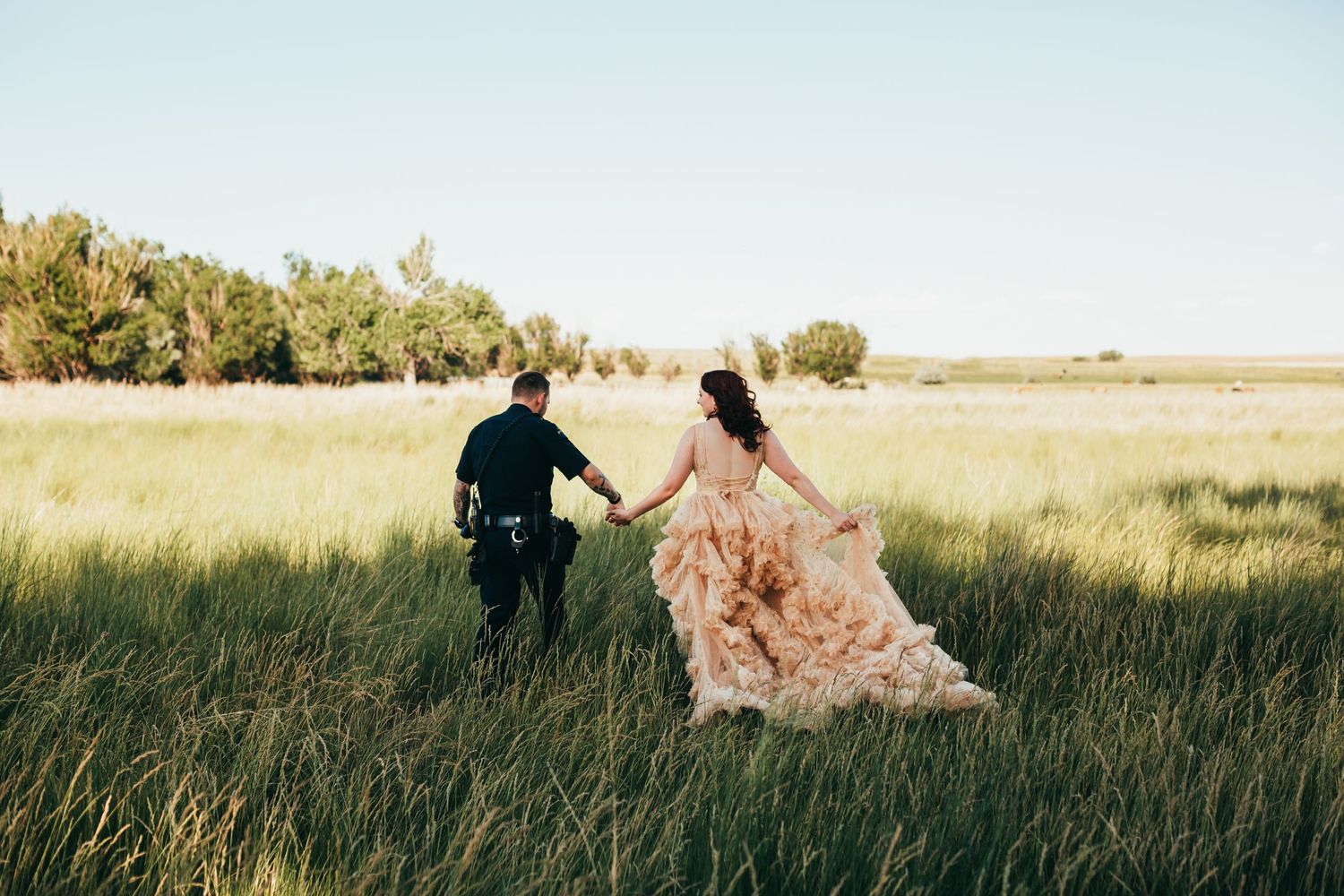 Couple walking through tall grass field with mountains in background during sunset.