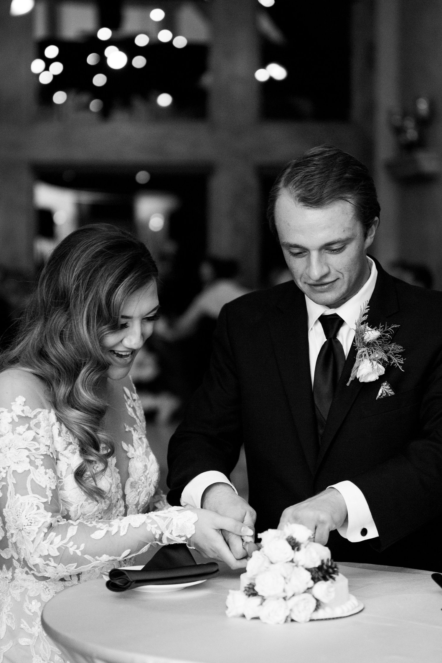 Black and white photo of newlyweds cutting their wedding cake during reception.