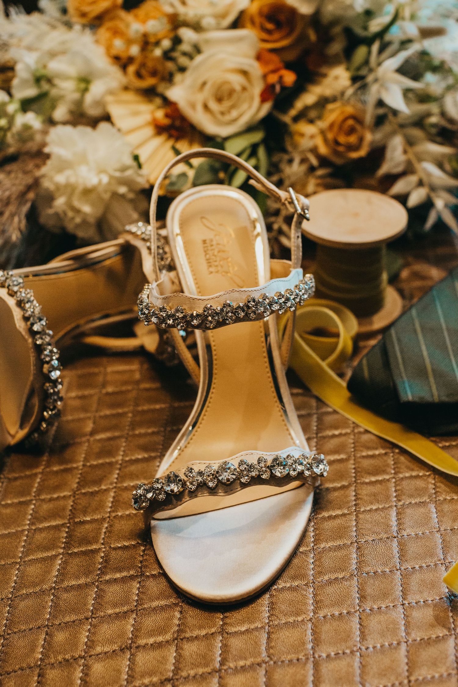 Crystal-embellished bridal sandals with floral bouquet in warm golden tones.