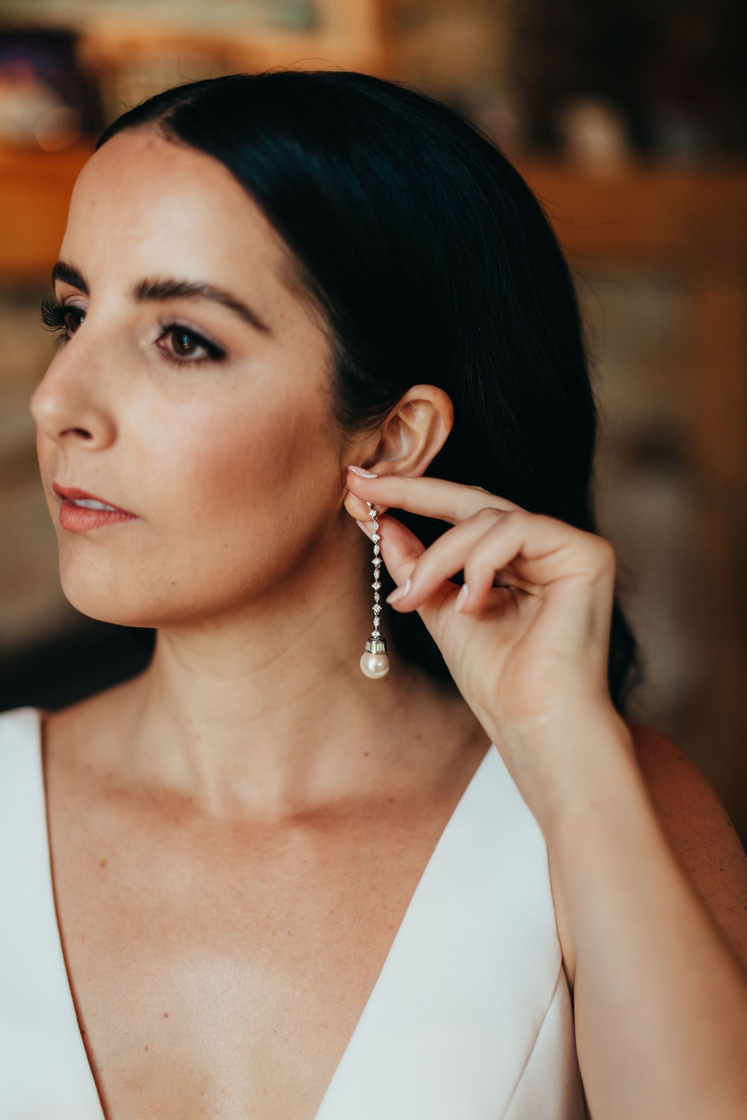 Close-up of pearl drop earring being put on by woman in white dress.