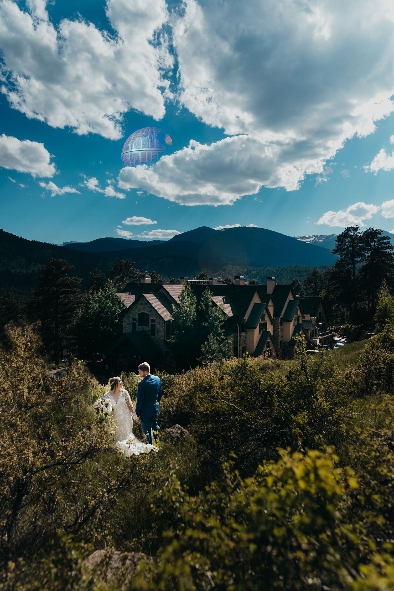 A scenic mountain wedding photo with dramatic clouds and mountain lodge buildings in the background.