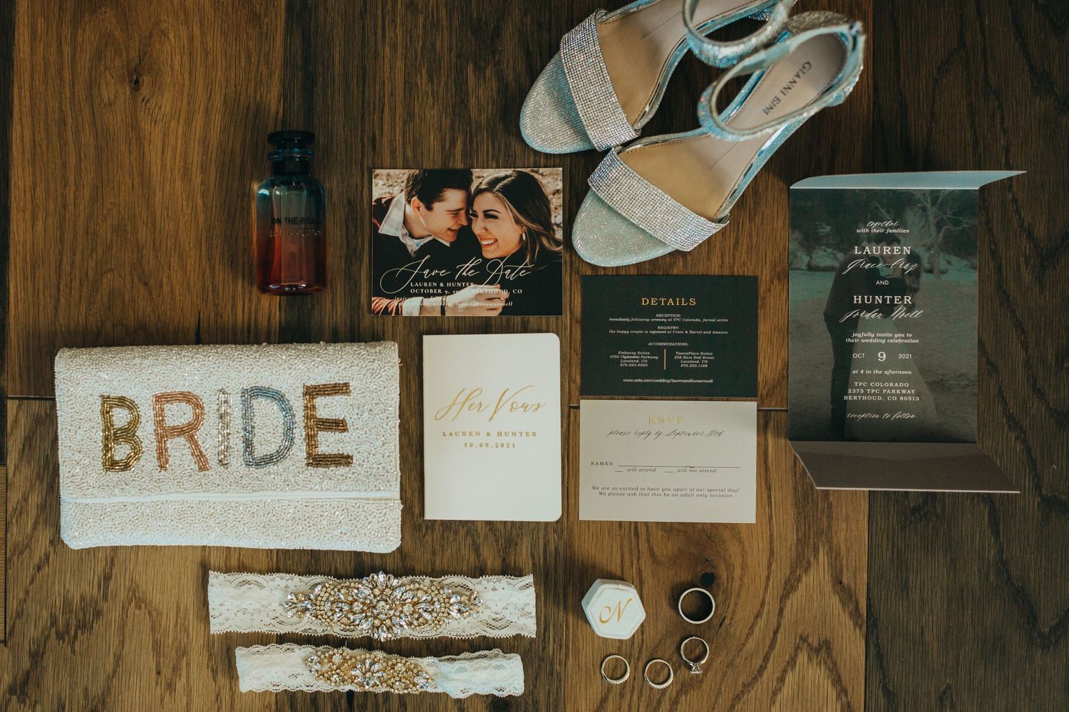 Wedding details flatlay with invitation suite, shoes, rings and 'BRIDE' text on wooden surface.