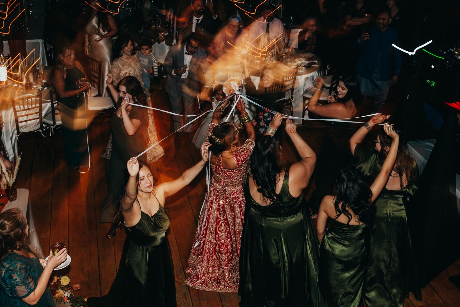 Wedding reception dancing with celebrants in dark green dresses and red attire.