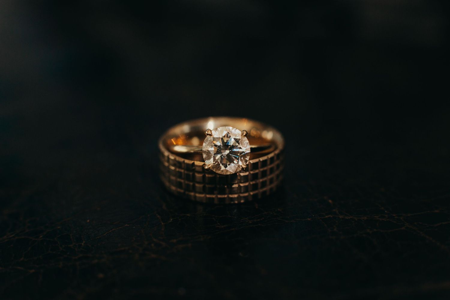Gold wedding and engagement rings with diamond on dark background.