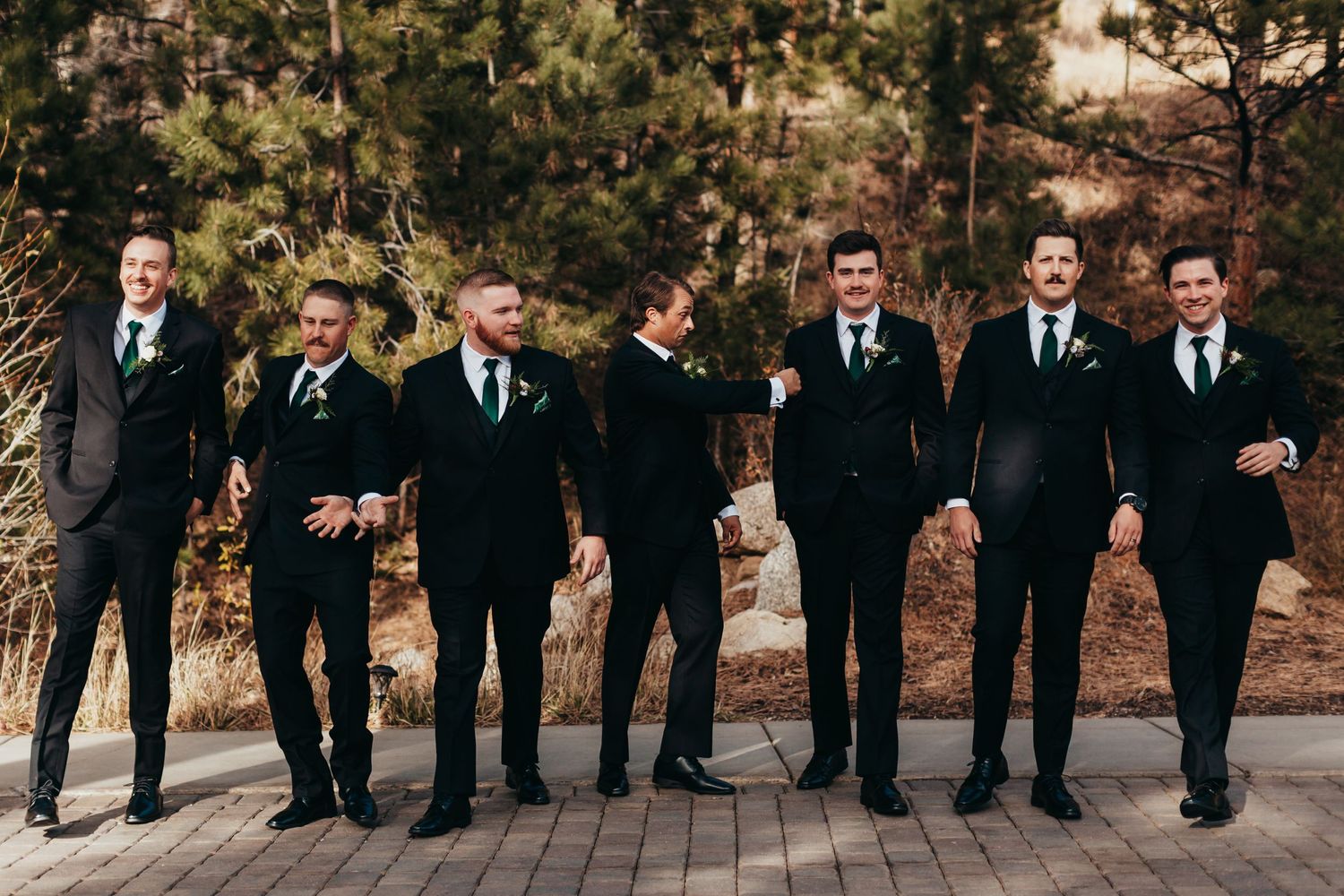 Groomsmen in black suits stand together on brick patio for formal wedding photo.