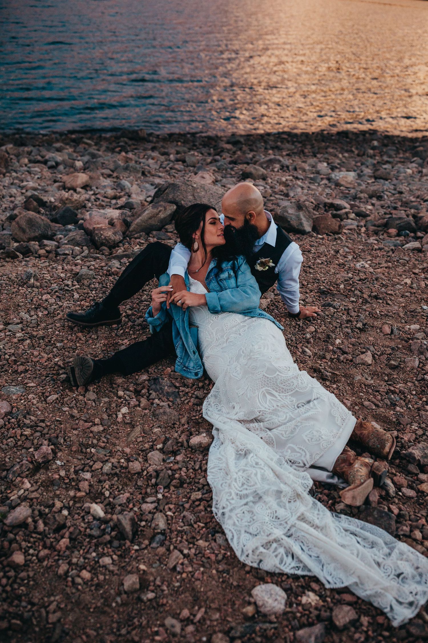 Romantic sunset moment of newlyweds relaxing on rocky lakeshore.