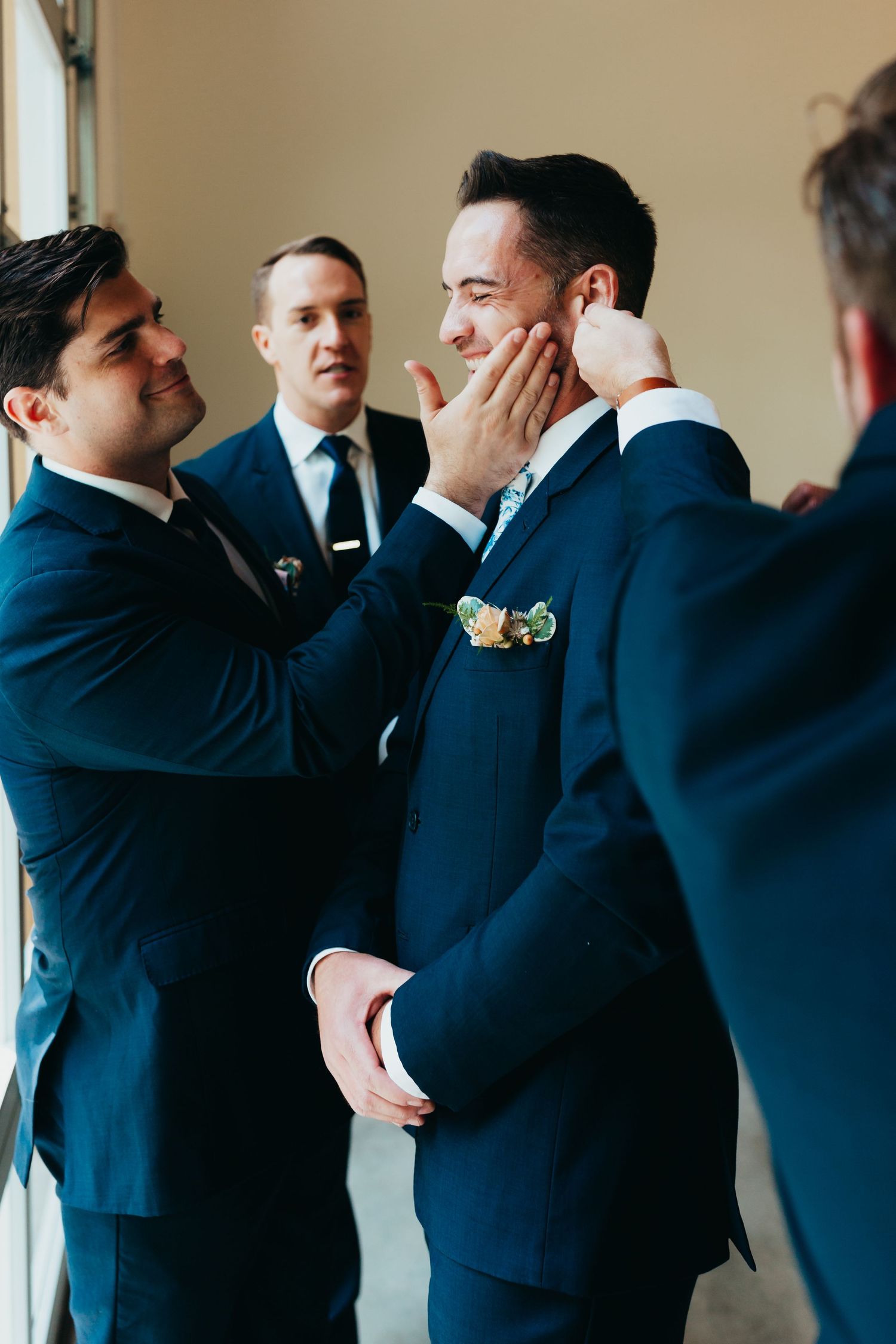 Groomsmen in navy suits sharing an emotional moment before the wedding ceremony.