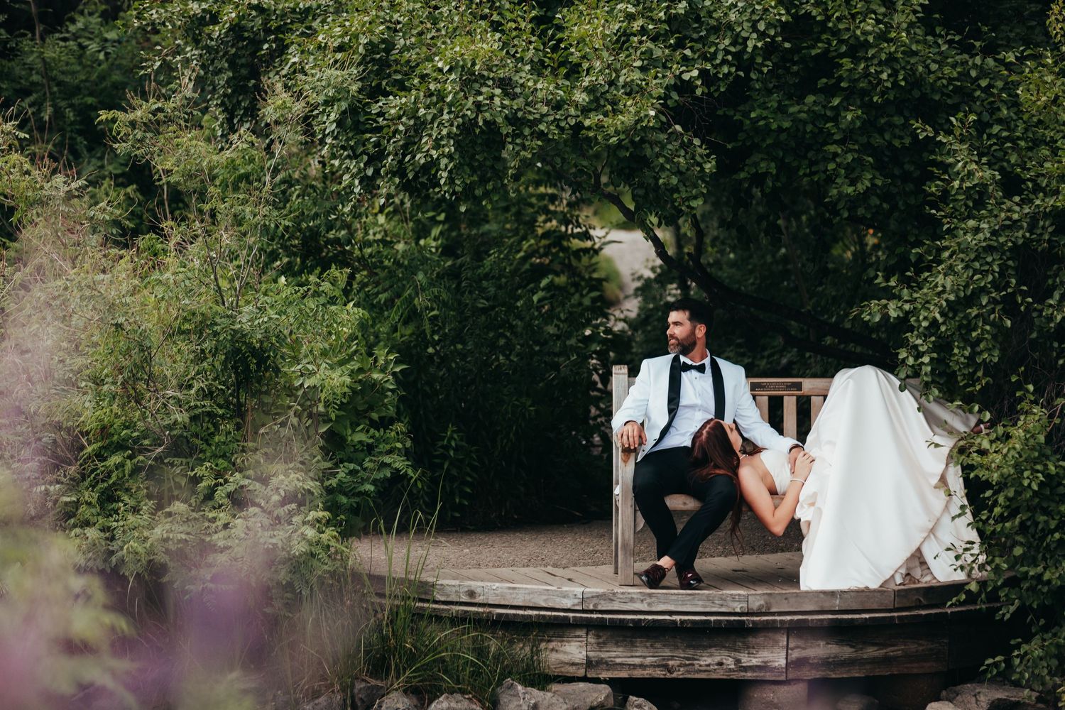 Couple shares romantic moment on rustic wooden dock surrounded by greenery.