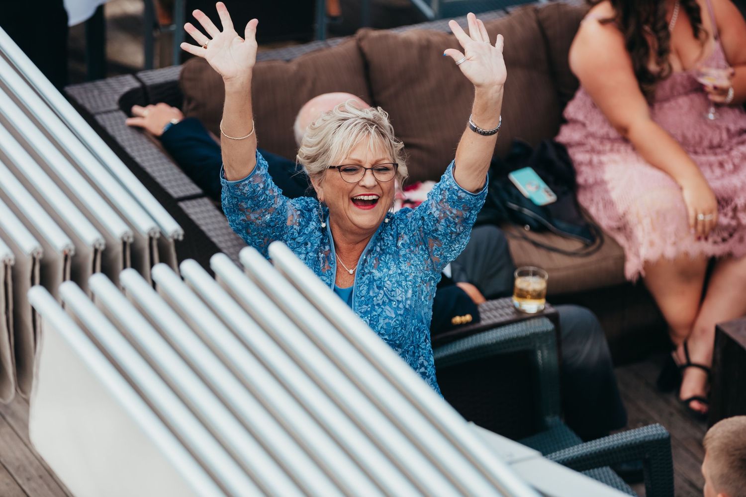 Wedding guest in sparkly blue dress raises arms joyfully during celebration.