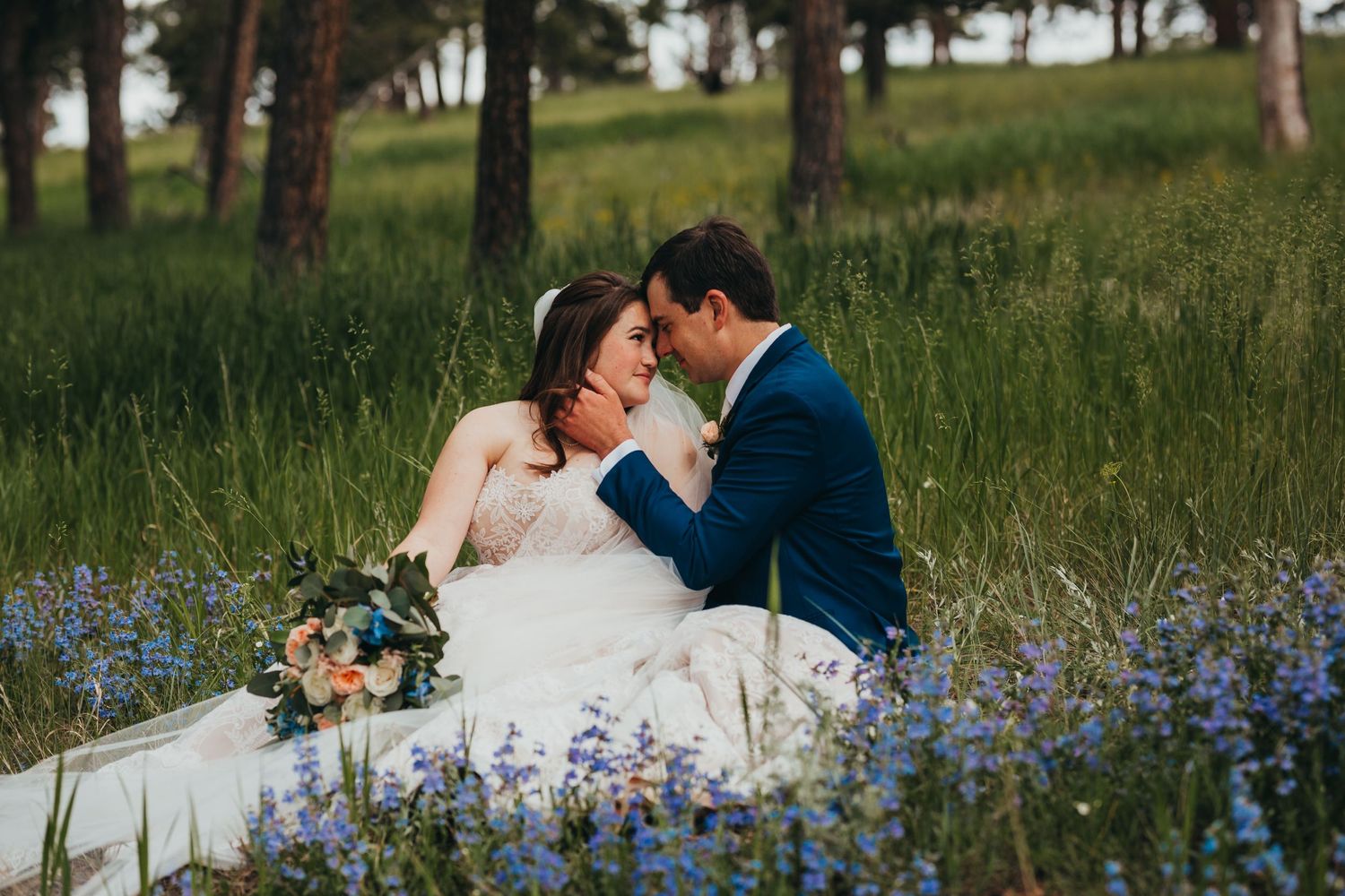 Couple shares intimate moment while sitting among purple wildflowers in mountain meadow.
