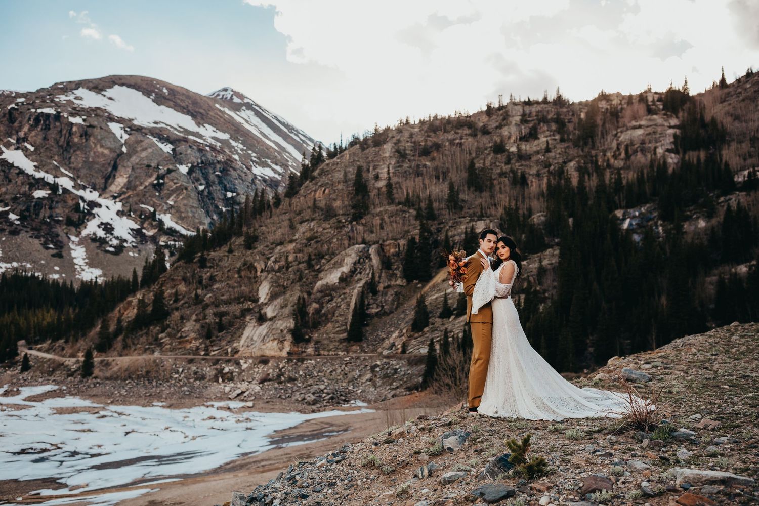 A scenic mountain wedding photoshoot with snow-capped peaks and rugged terrain in the background.