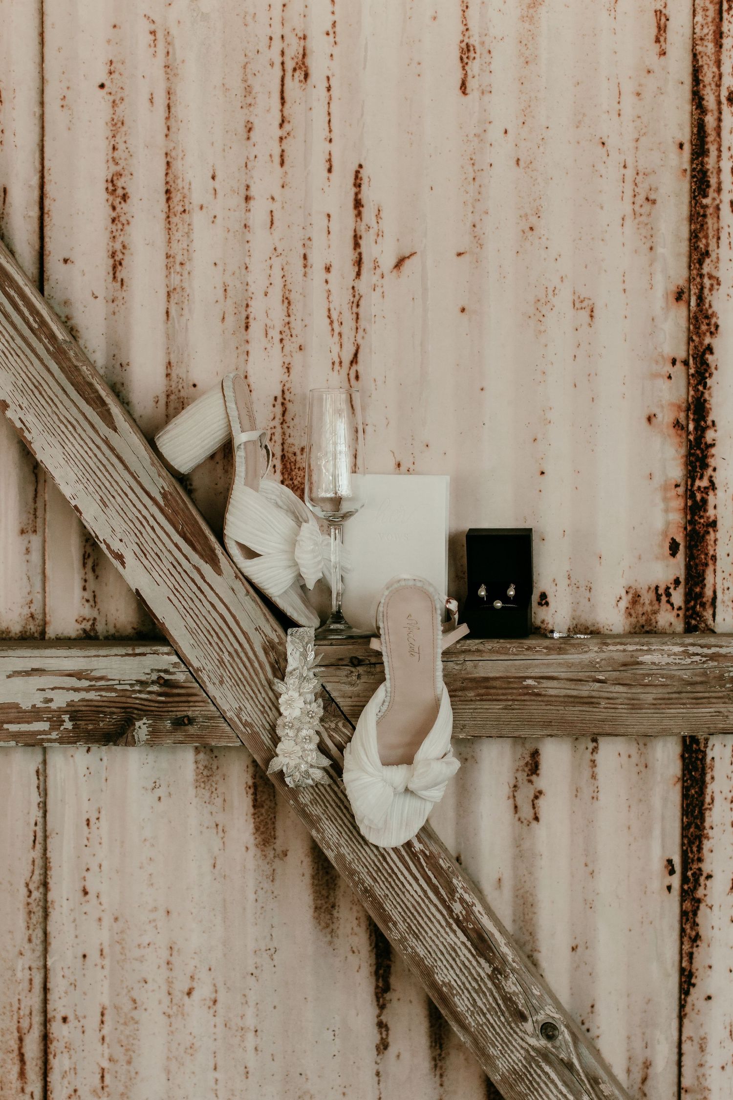 Elegant white bridal shoes displayed on weathered wooden beams against rustic metal wall.
