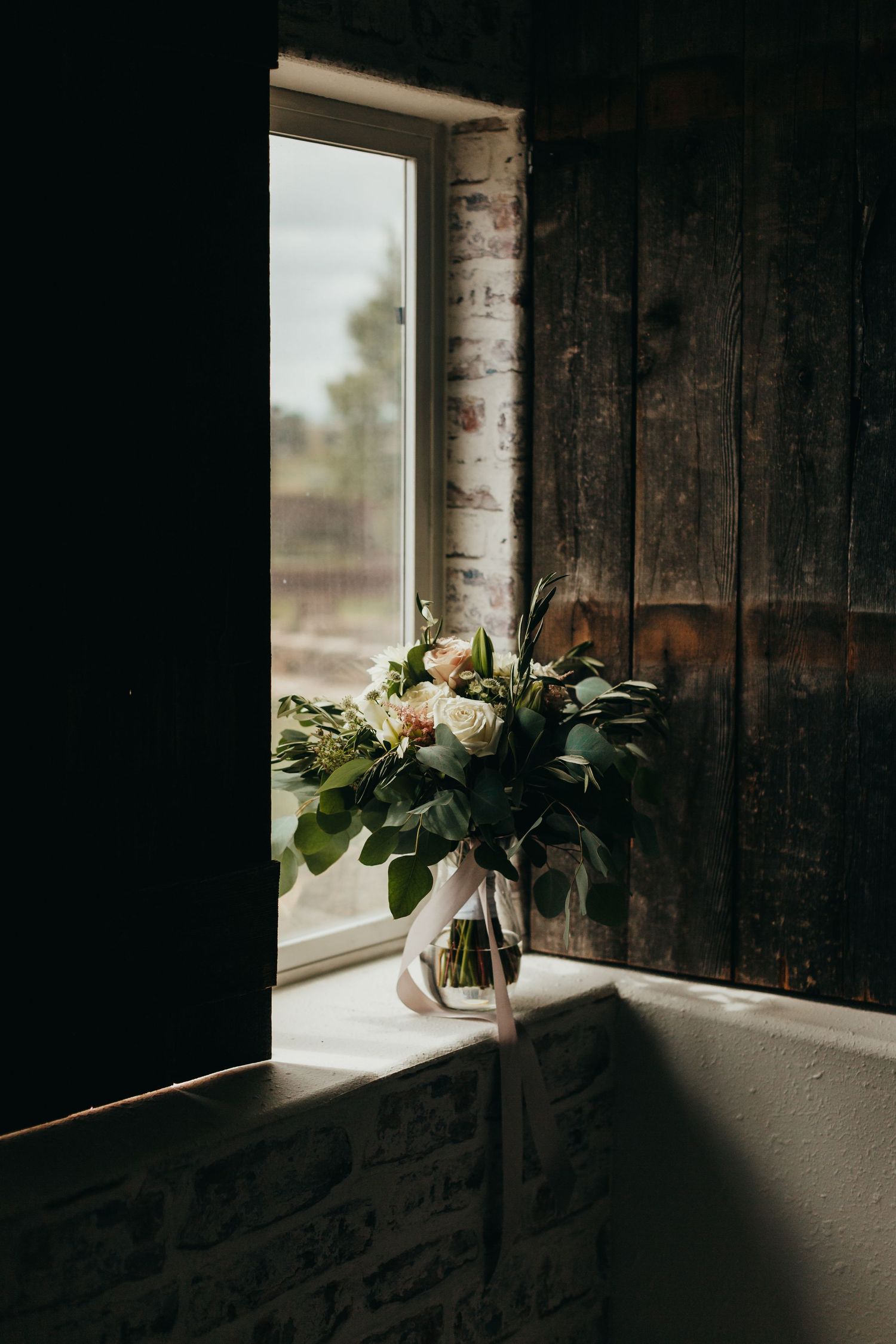 A romantic floral arrangement in a vase sits by a rustic window with natural light streaming in.