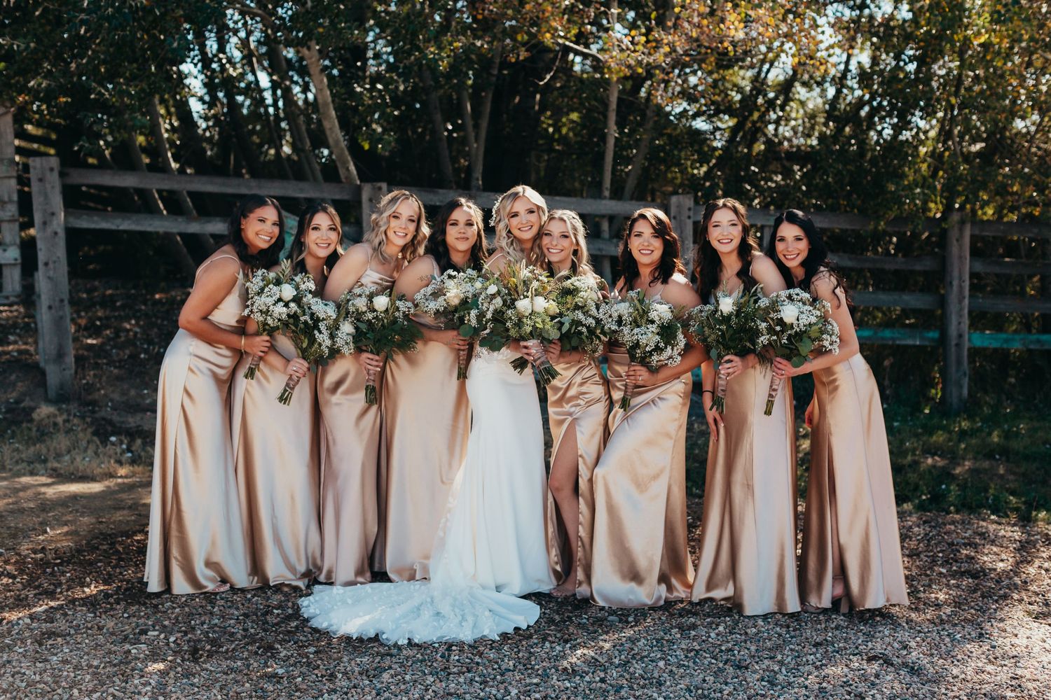 Bridal party in champagne dresses poses with bride in white gown holding floral bouquets.
