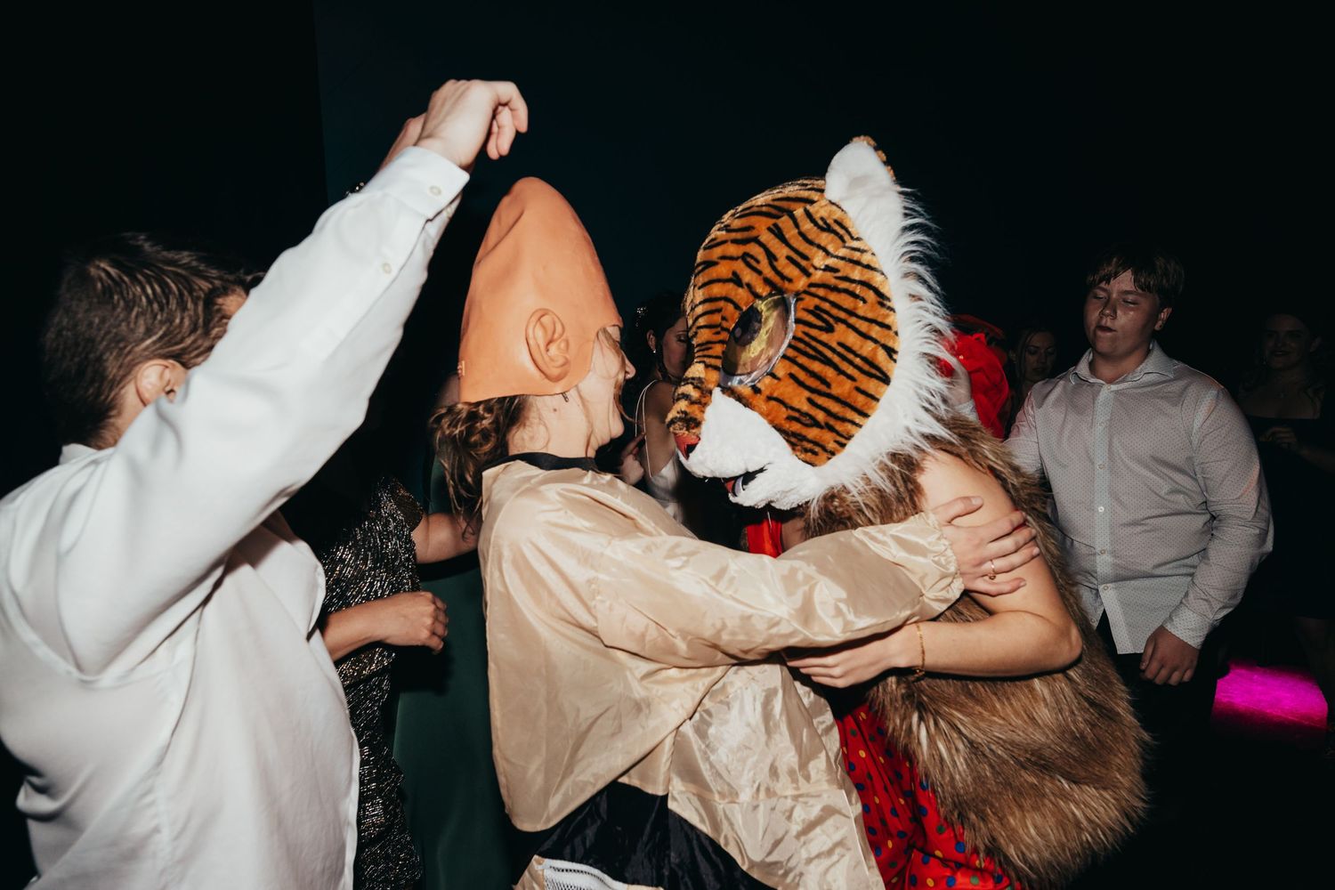 Party guests dancing with someone in tiger mascot costume at reception.