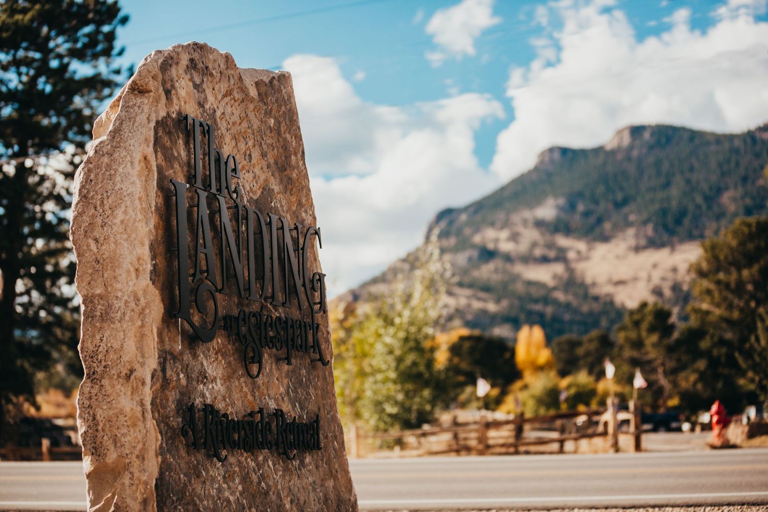Large stone monument against mountain backdrop with blue sky and autumn trees.