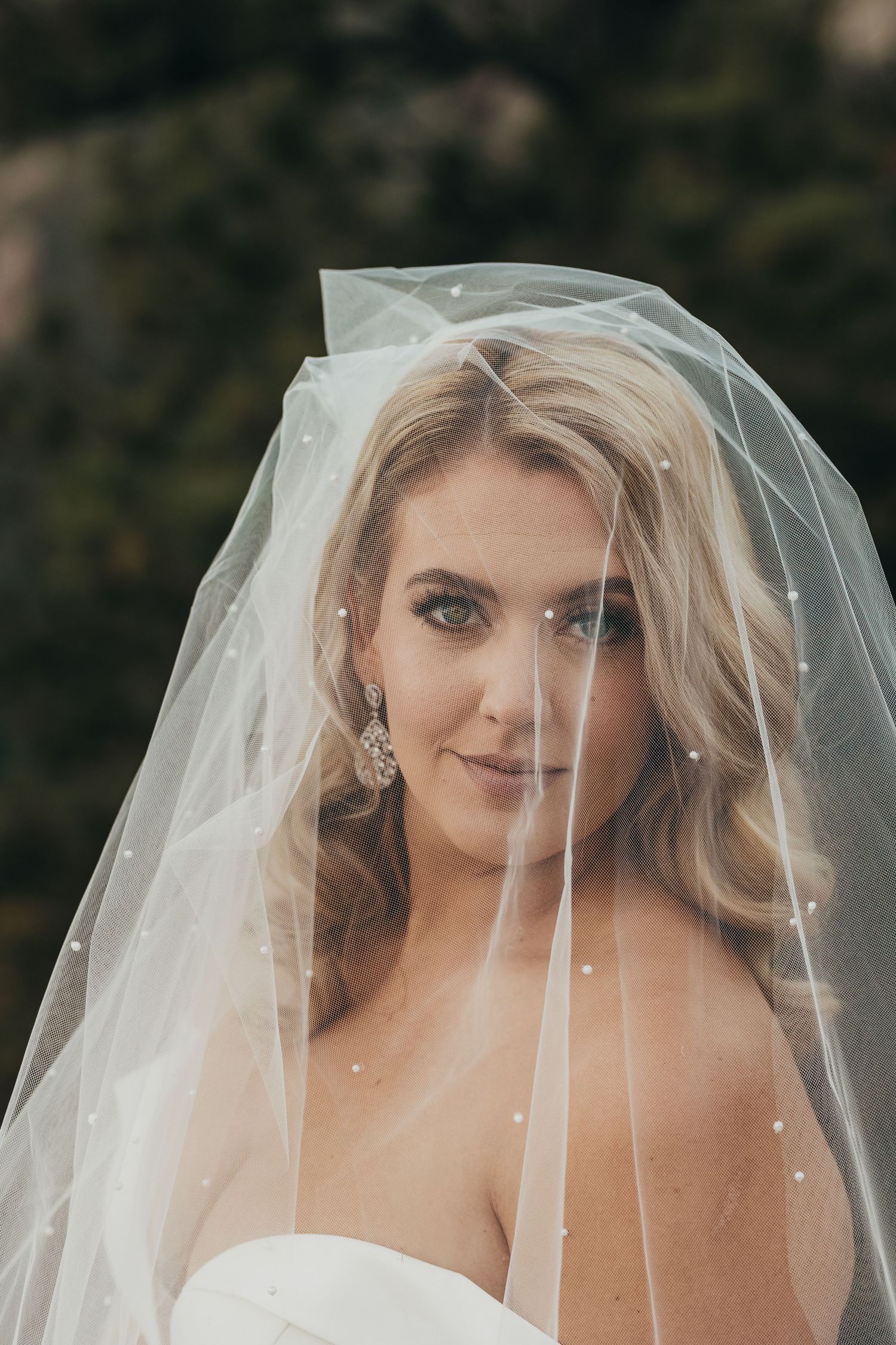 Bridal portrait with flowing veil and pearl details in natural setting.
