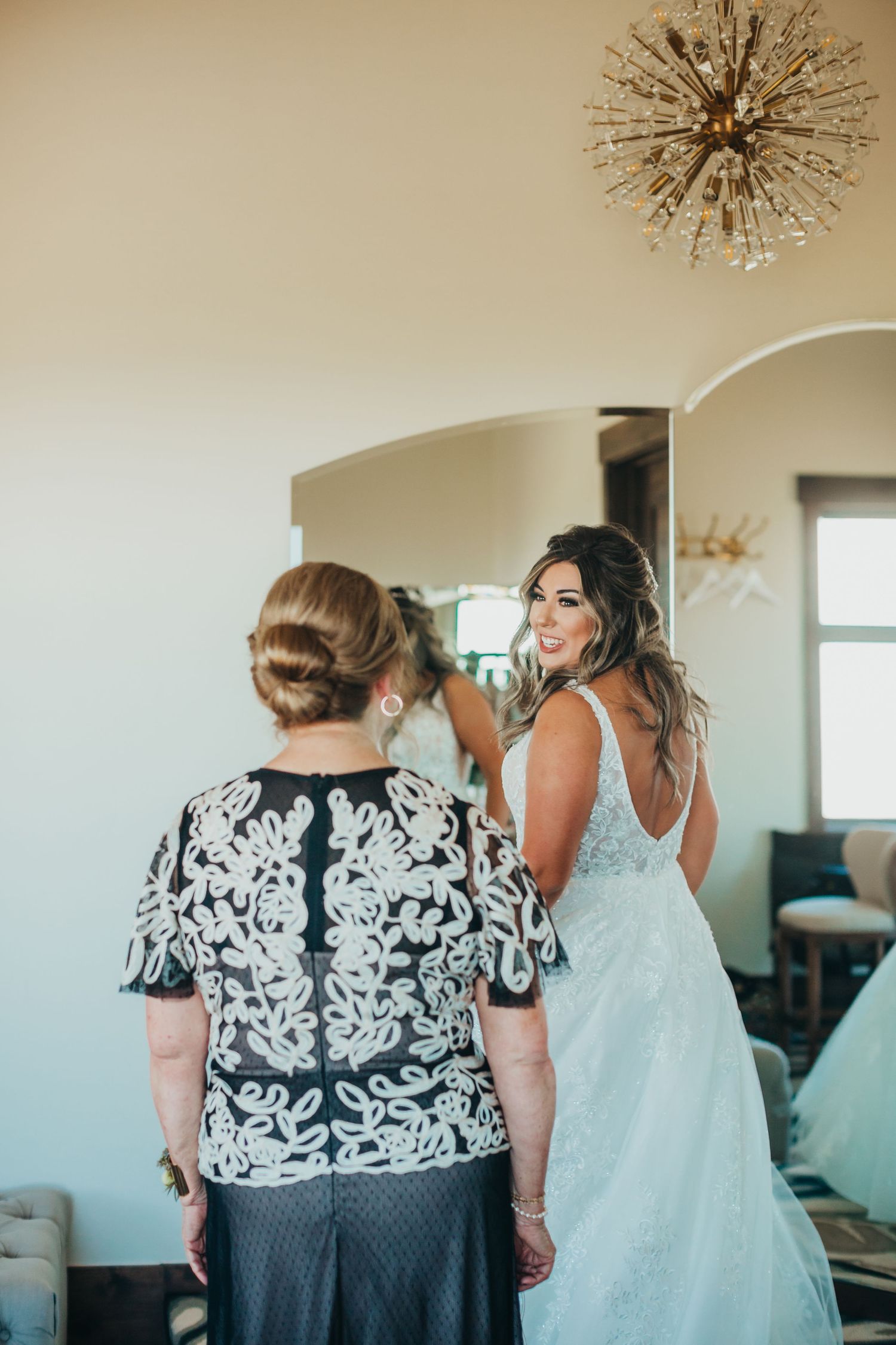 A person in a white lace wedding gown being helped with final preparations.