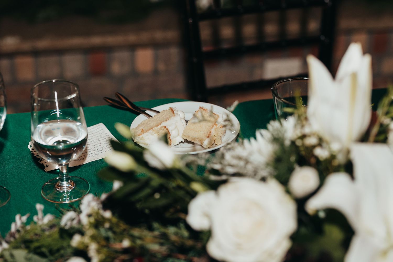 An elegant table setting with wine glasses, white flowers and greenery on a dark green tablecloth.