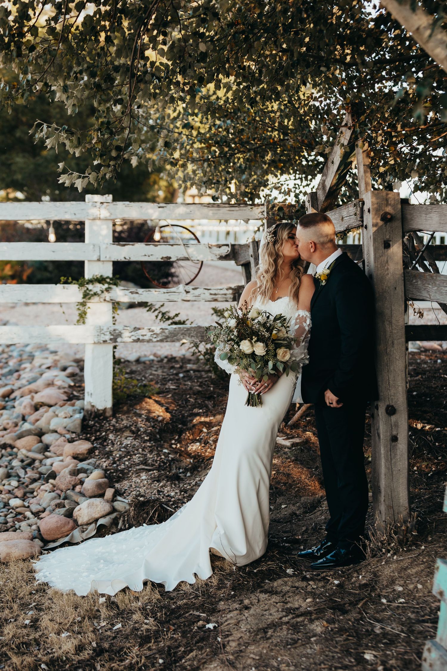 Intimate wedding couple moment captured by white fence with elegant bridal bouquet.
