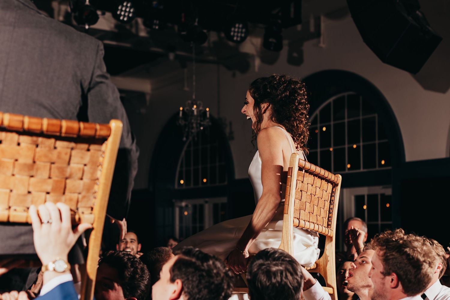 Lively wedding reception crowd lifting chairs during celebration.