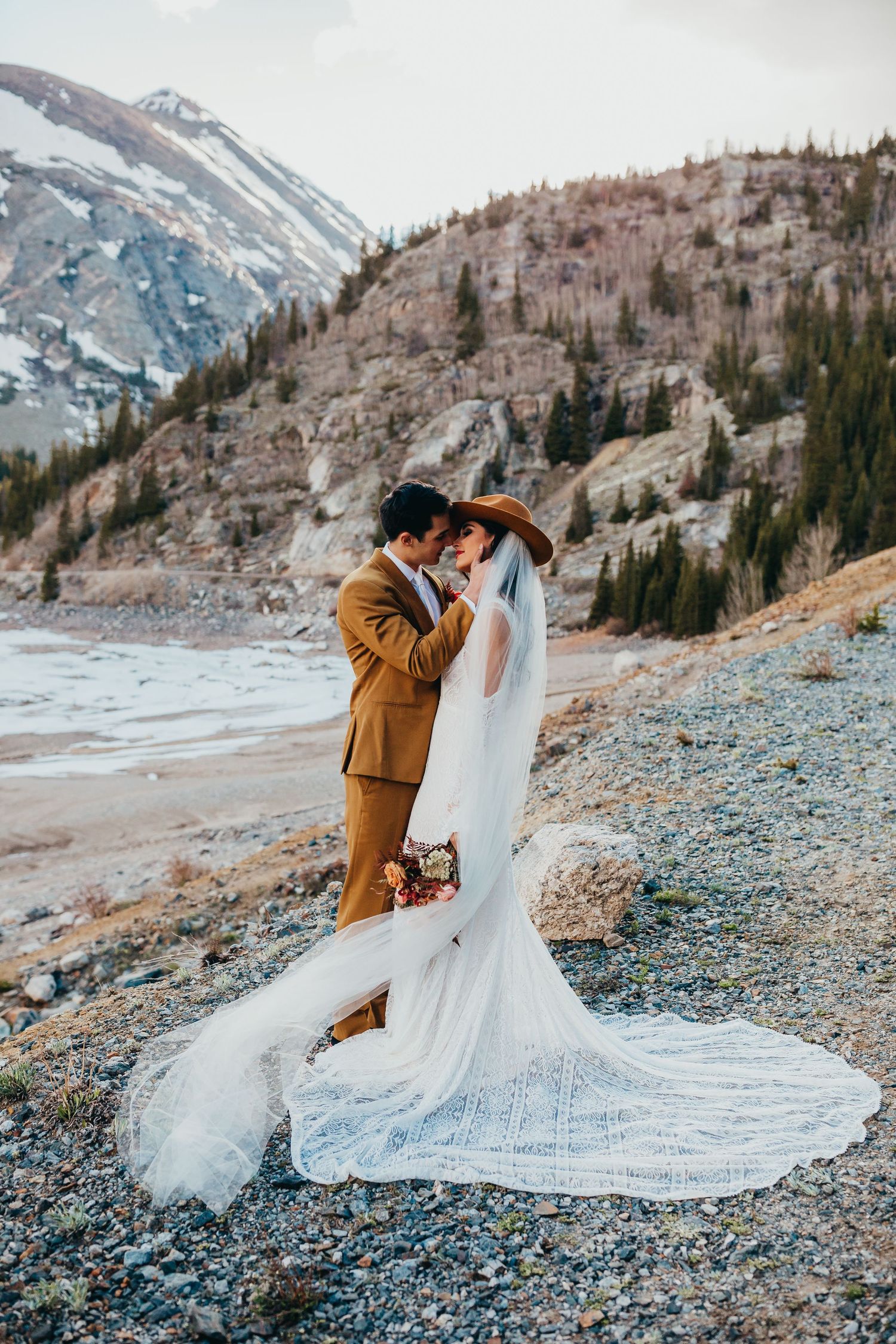 An intimate mountain wedding portrait with a long lace train dress and camel-colored suit.