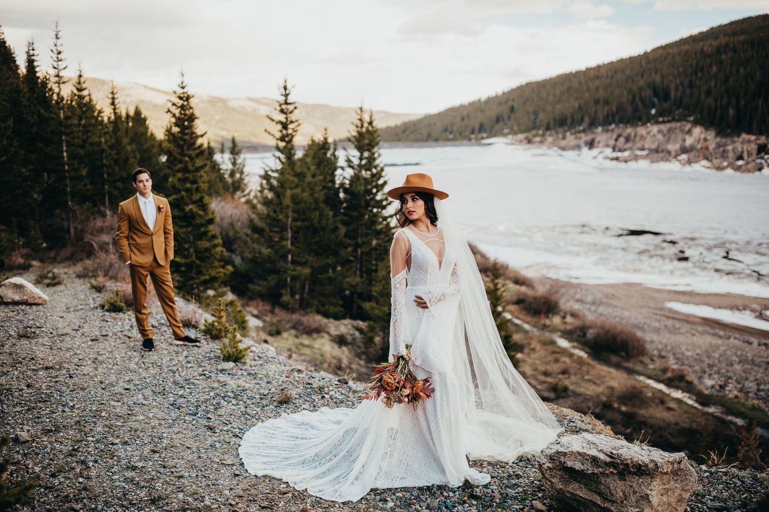 Wedding couple poses on mountain trail overlooking snowy winter lake.