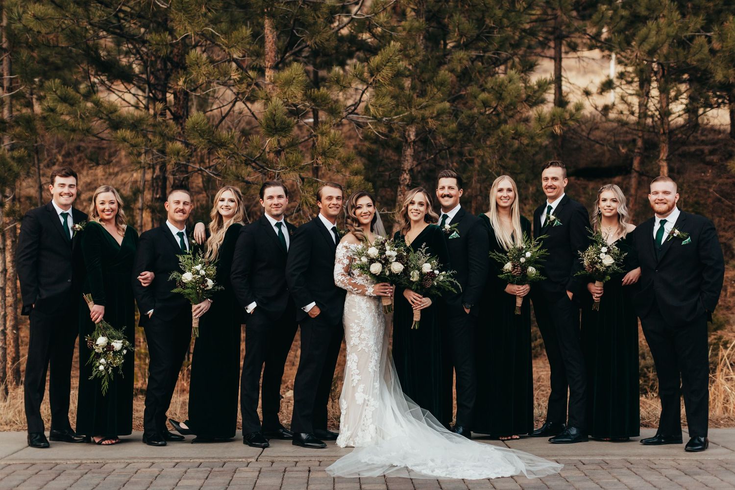 Full wedding party in black and white attire poses formally on brick patio.