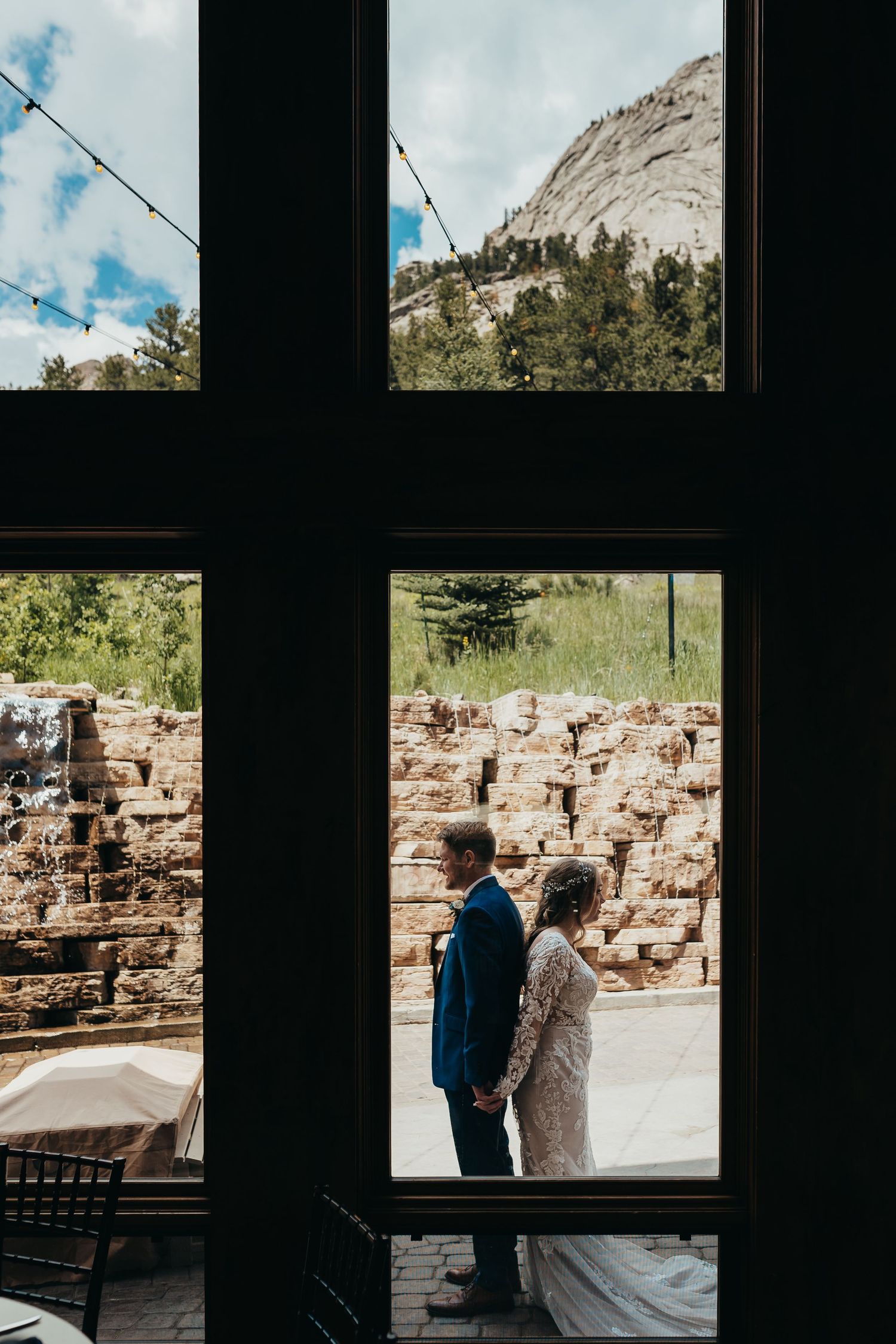 A couple stands framed through a window with a majestic mountain and stone wall backdrop.