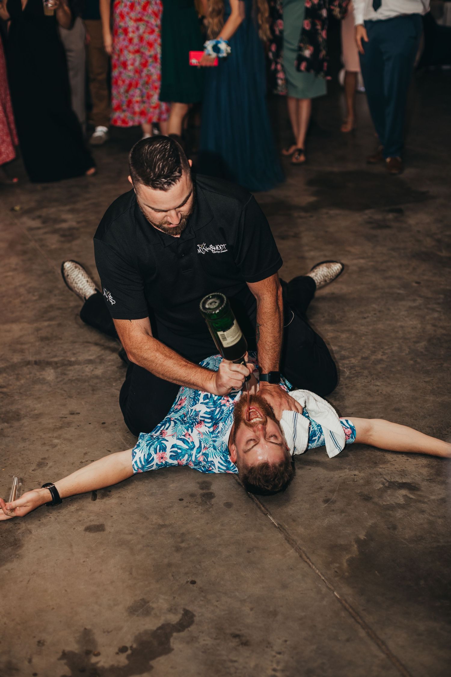 Man pours champagne into person lying on dance floor at wedding reception.