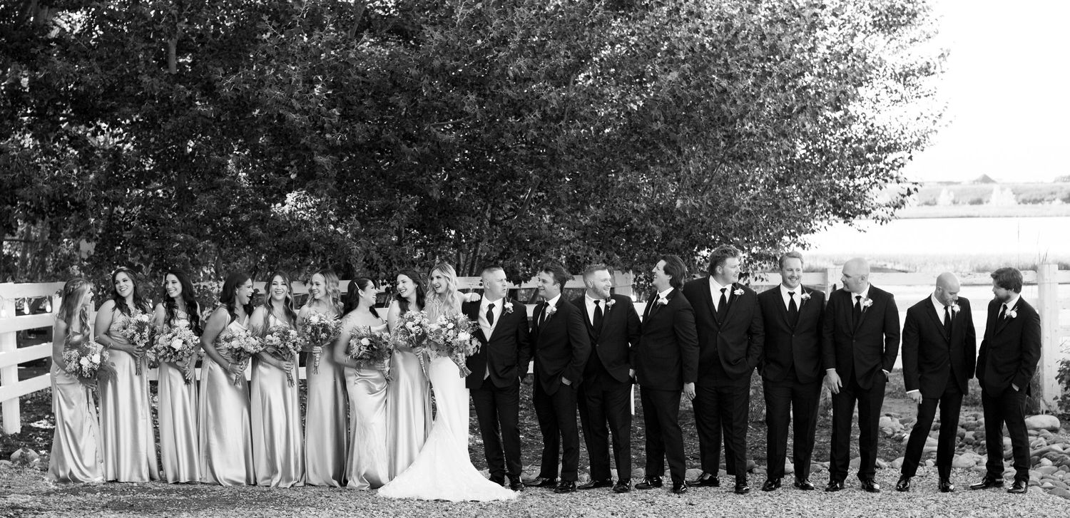Black and white photo of wedding party lined up outdoors with bridesmaids and groomsmen.