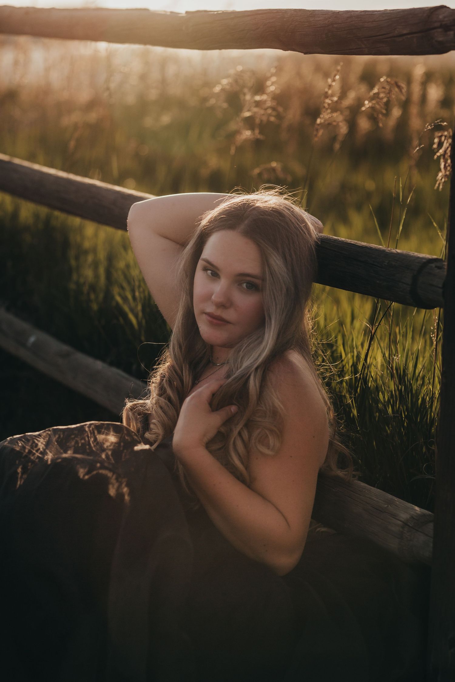 Dreamy golden hour portrait by wooden fence in tall grass field at sunset.