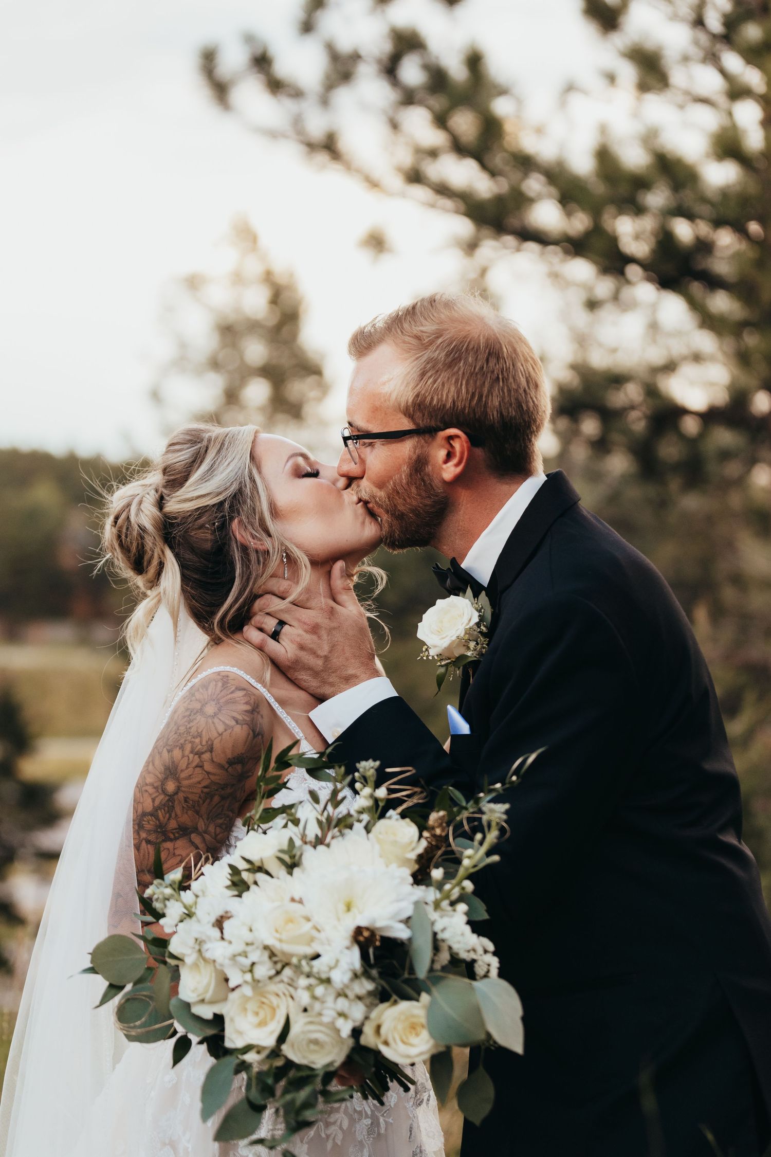 Romantic wedding portrait with white floral bouquet against natural outdoor backdrop.