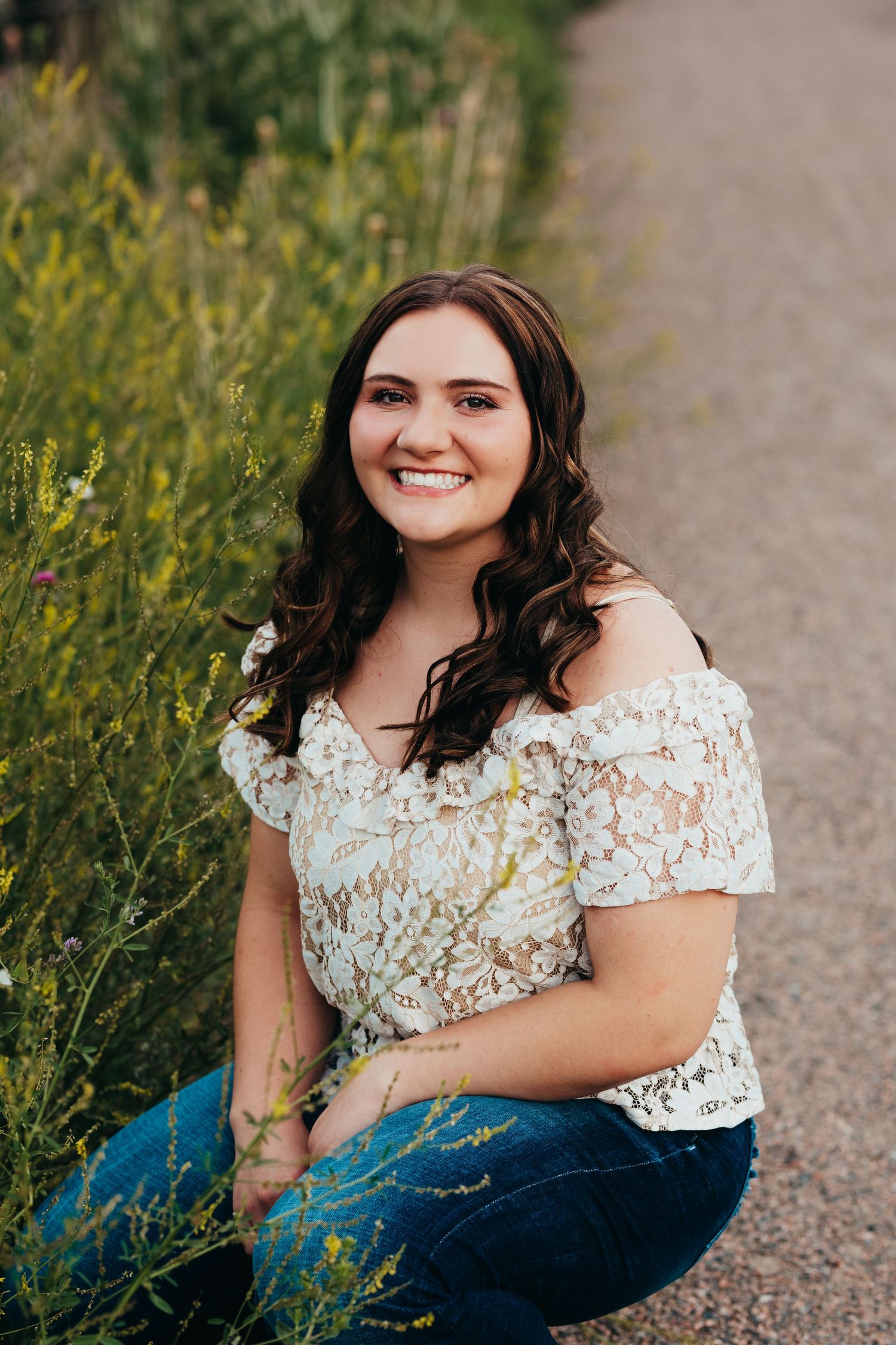 Portrait of someone in a white lace top sitting among yellow wildflowers.