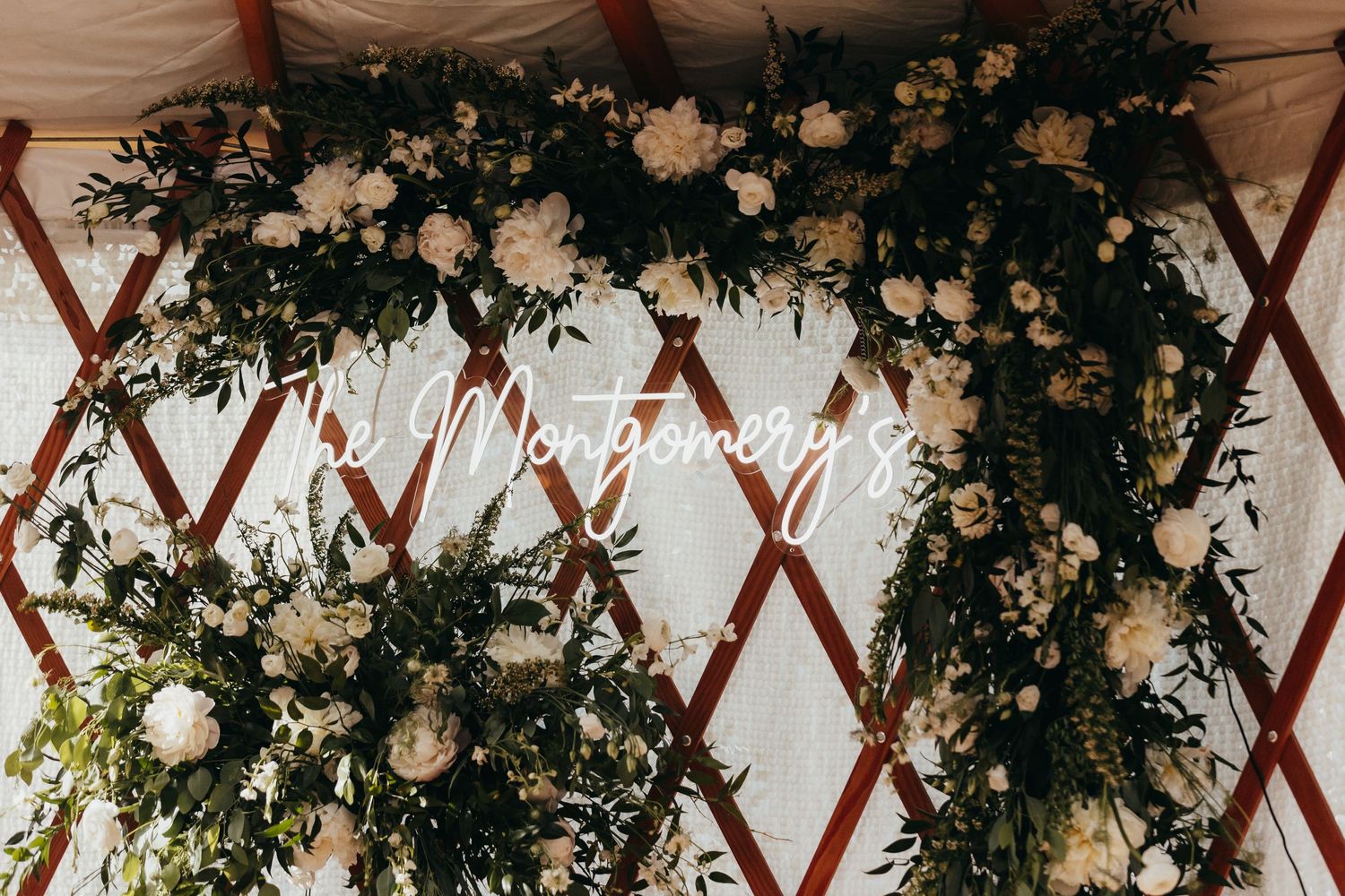 Elegant floral arch with white roses and greenery decorates a white tent structure.