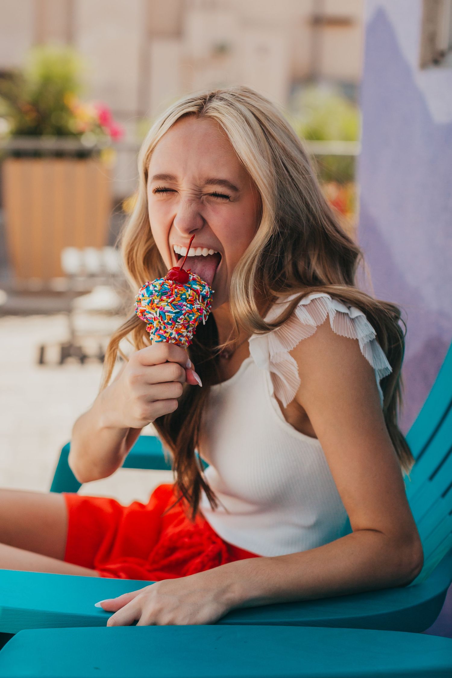 Person enjoying a colorful ice cream cone while relaxing on a bright turquoise lounge chair.