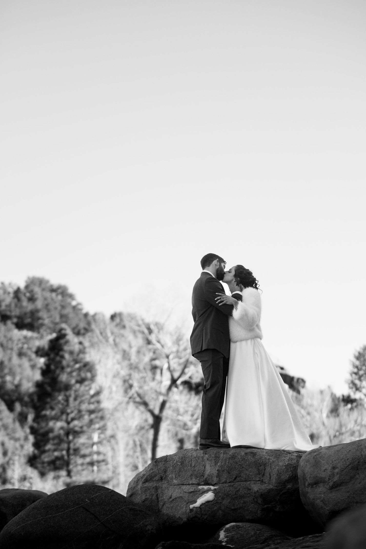 A romantic black and white wedding photo of a couple standing on a rocky outcrop against a mountainous backdrop.