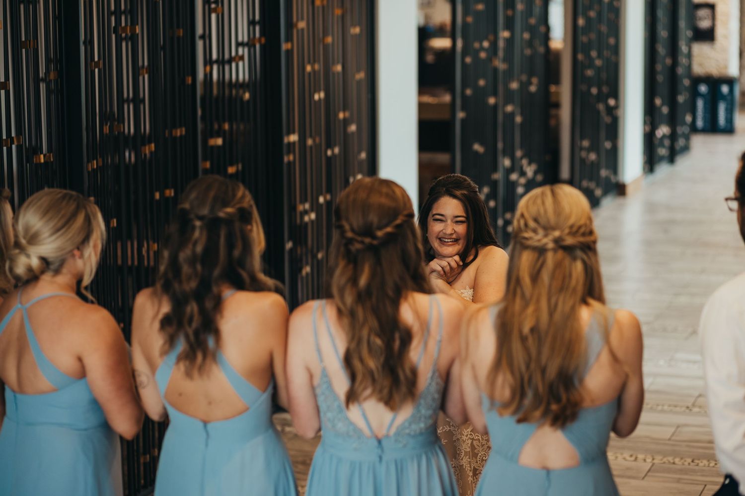 Bridesmaids in light blue dresses walk together down modern hallway.