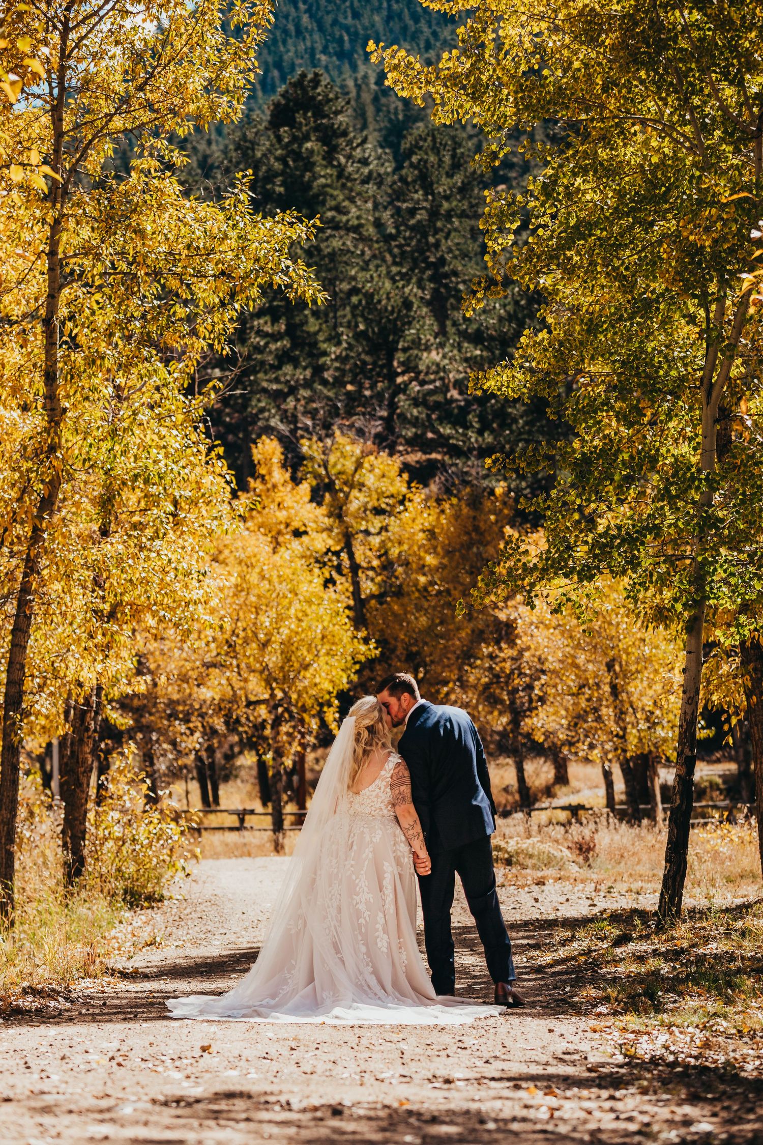 Newlyweds walking down path surrounded by golden fall foliage.