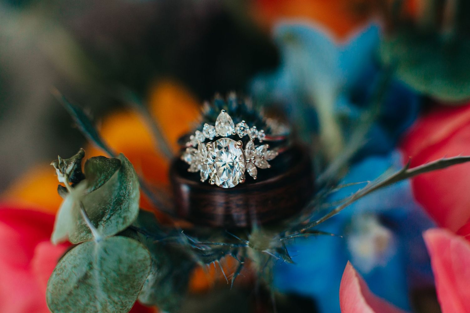 Sparkling diamond engagement ring nestled among colorful flowers in a macro shot.