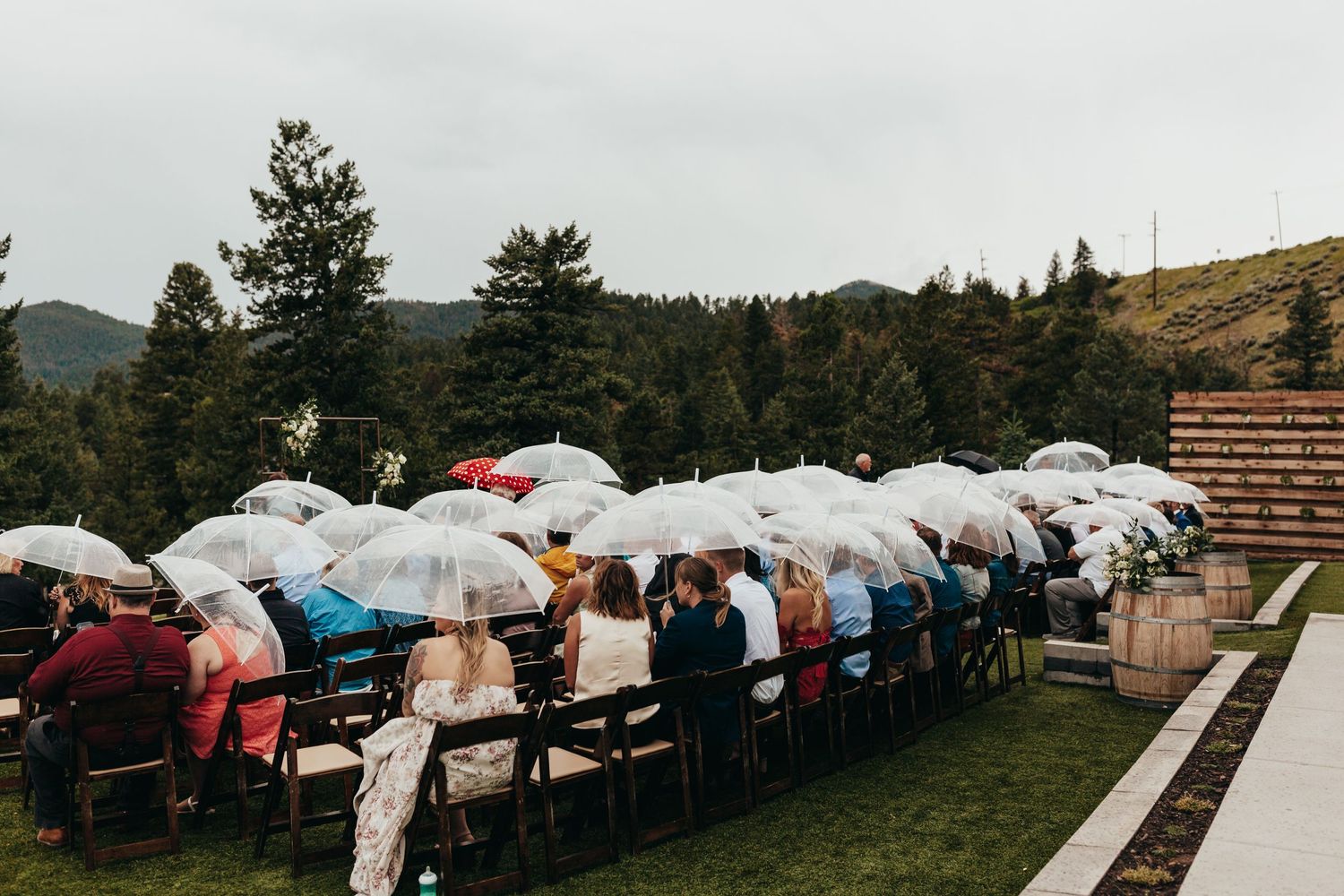 Wedding guests huddle under white umbrellas during an outdoor rainy ceremony.