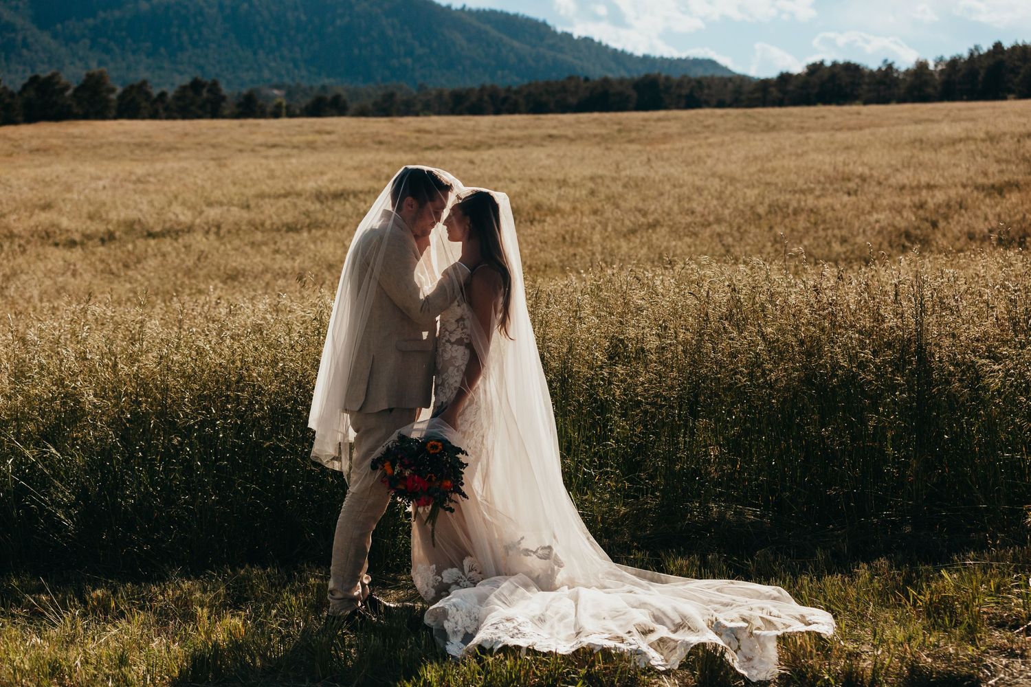 Couple shares intimate moment in flowing wedding attire against mountain landscape.