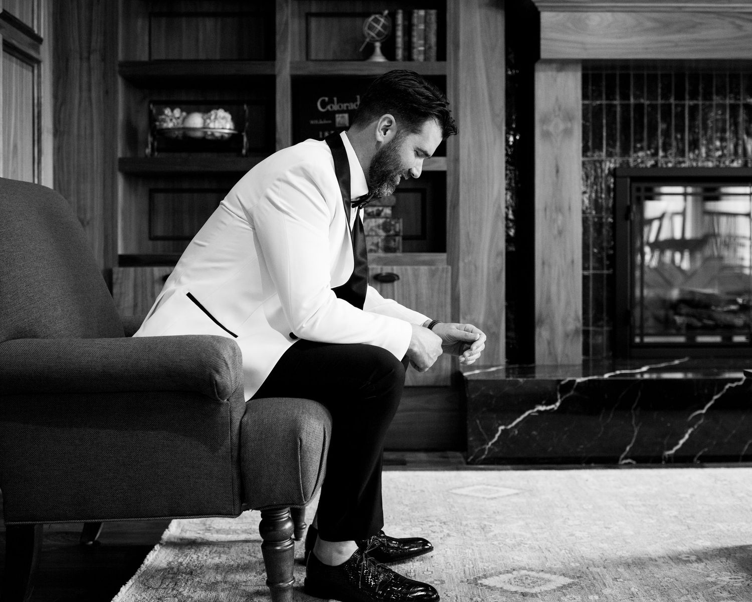 A person in formal attire sits pensively on a couch in a black and white photo.