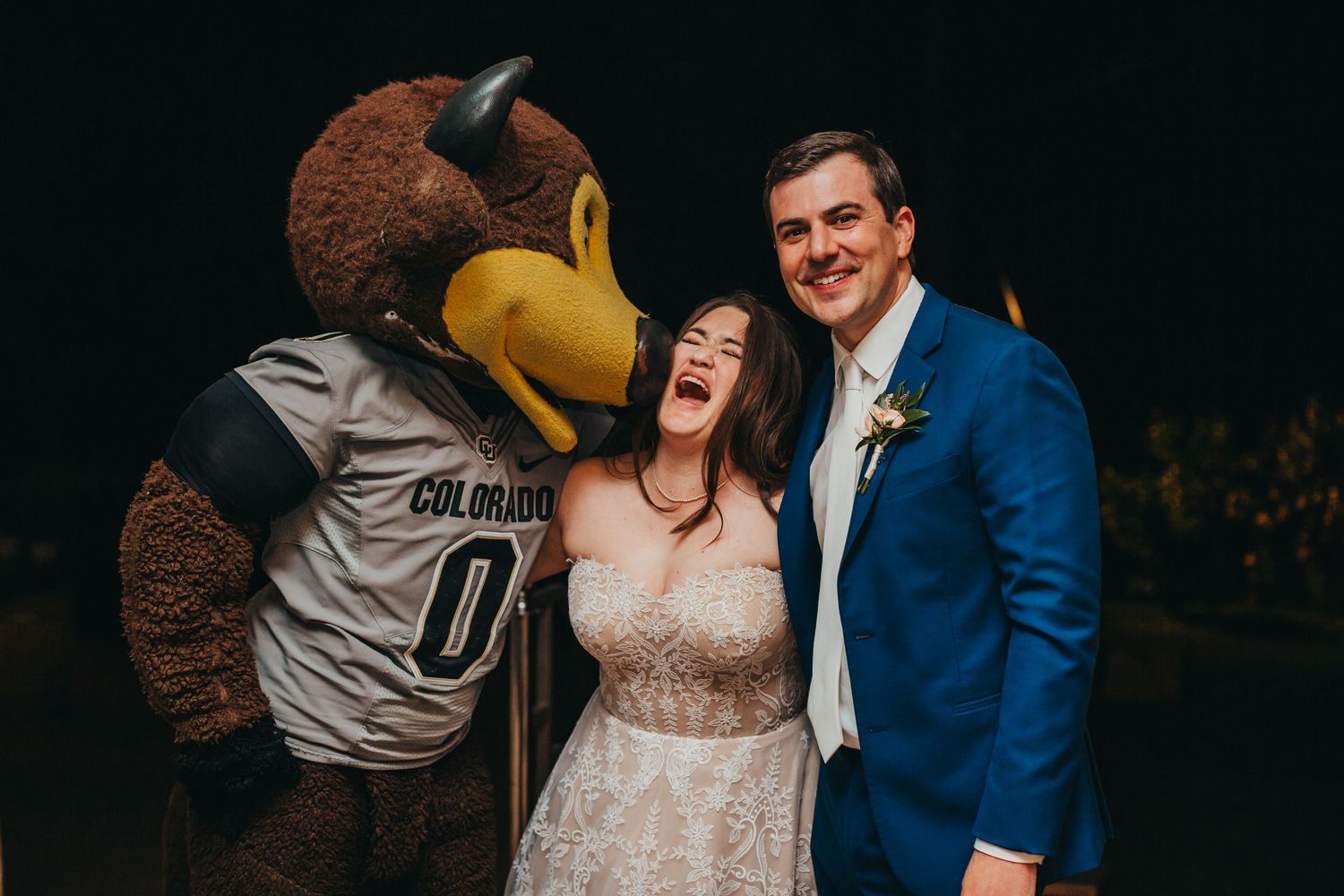 A mascot in a sports jersey poses with a couple during a celebratory wedding moment.