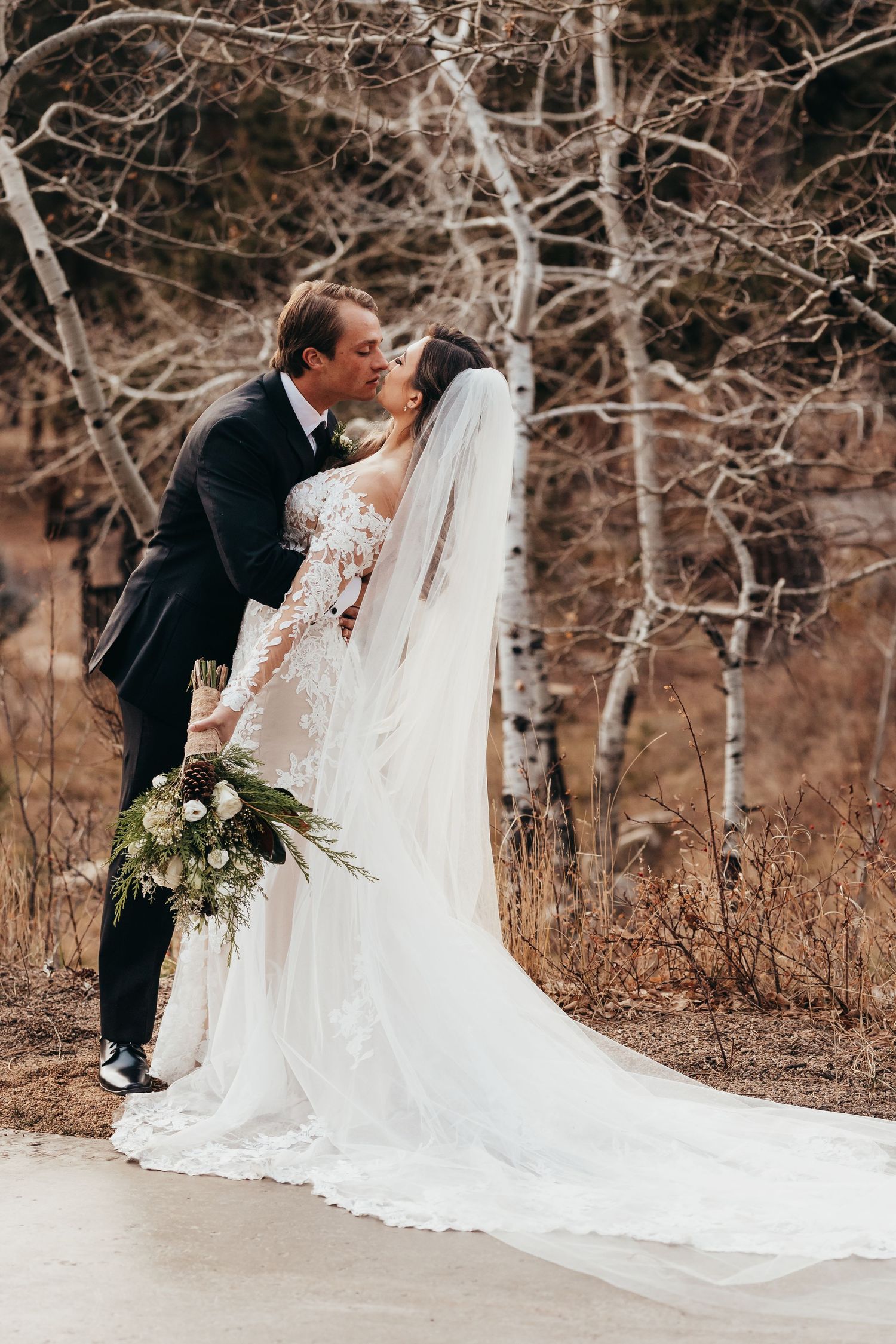 Romantic wedding photo of couple embracing among bare winter trees.